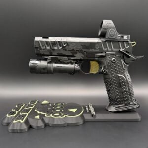 Detail shot of a camo-pattern pistol with a tactical grip and underside accessory, mounted on a decorative base with embossed yellow-green symbols.