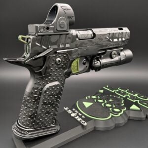 Detailed sci‑fi handgun on a display base, camo finish with tactical accessories and a bright green control panel nearby.