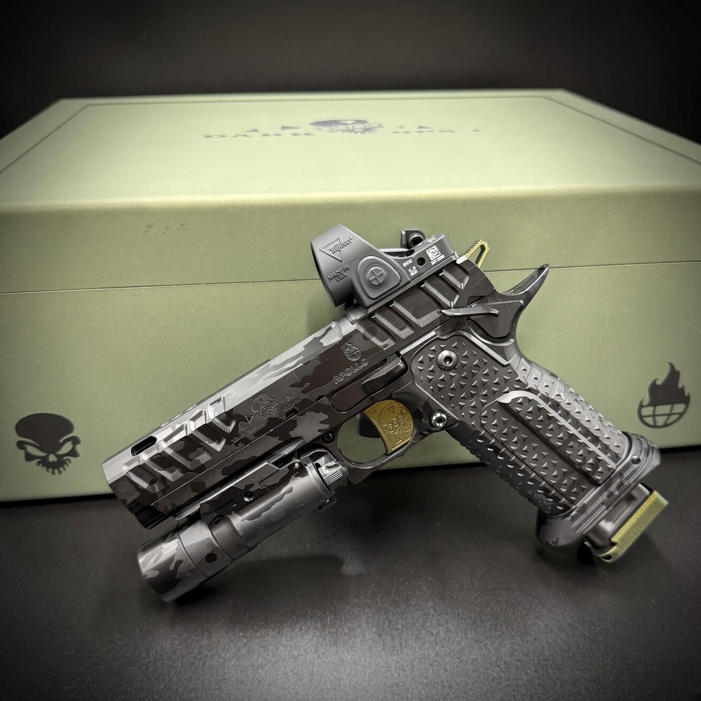 Camouflage-patterned tactical rifle with a red-dot sight, resting on a green storage case with a skull logo.