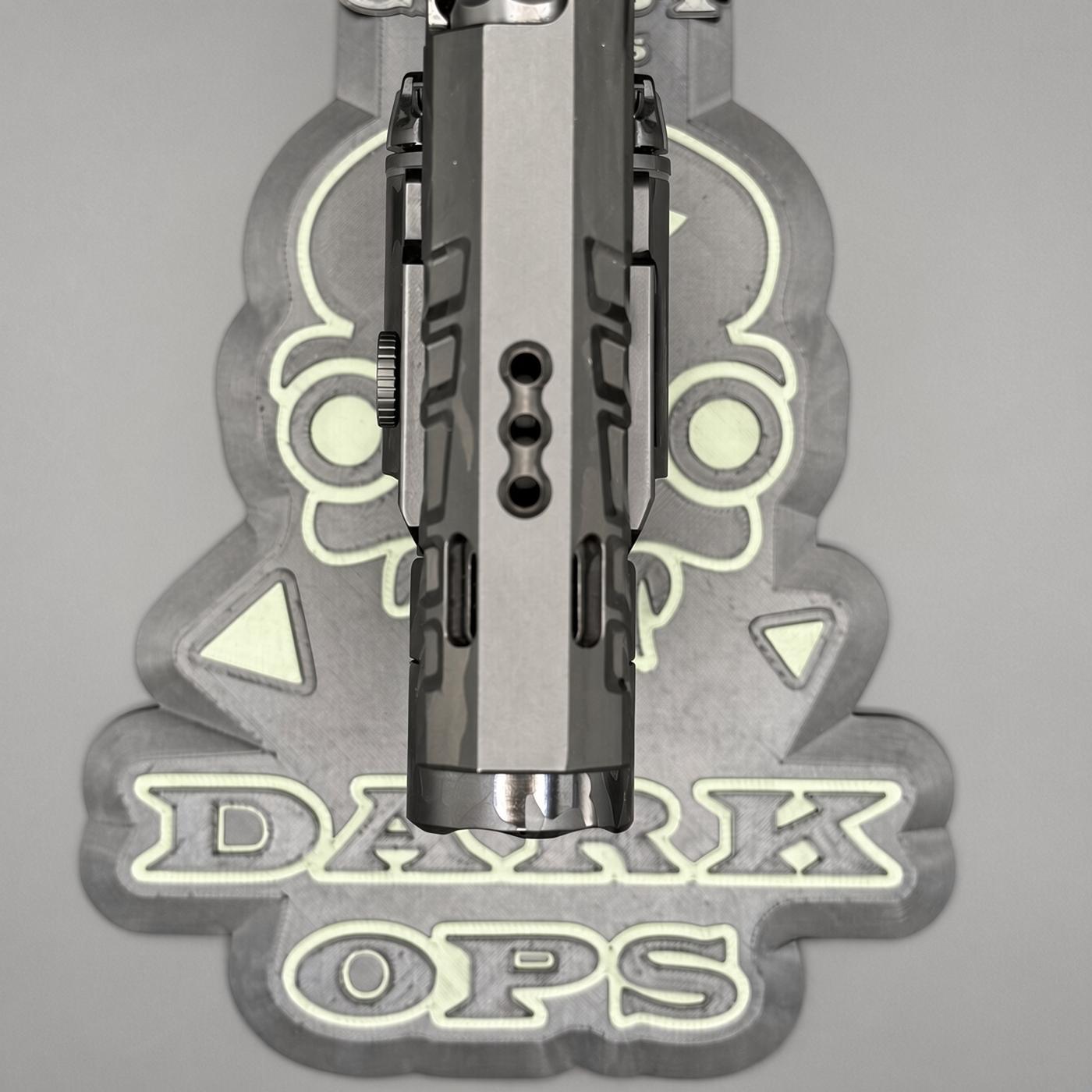 Close-up of a pistol slide mounted in a jig with a decorative 'DARK OPS' logo in the background.
